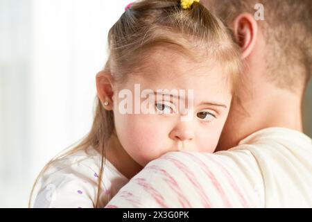 Primo piano di papà che tiene in mano una piccola figlia carina con la sindrome di Down che guarda lontano dalla telecamera, copia spazio Foto Stock