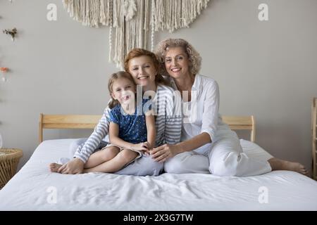 Bambina sua madre e la nonna che si abbracciano seduti sul letto Foto Stock