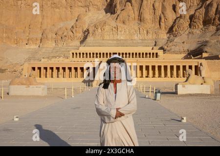 Un uomo egiziano in abbigliamento tradizionale all'ingresso del tempio mortuario di Hatshepsut a Deir el-Bahari (Governatorato di Luxor), in Egitto Foto Stock