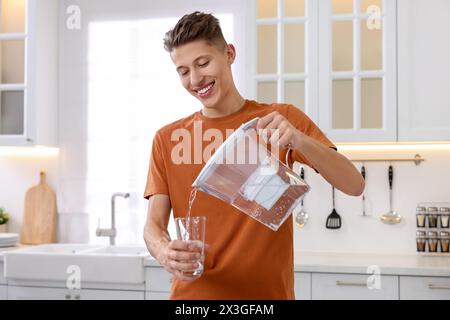 Uomo felice che versa acqua dalla caraffa del filtro in vetro in cucina Foto Stock