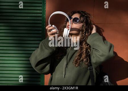 Giovane donna latinoamericana con capelli ricci che indossa le cuffie per strada Foto Stock