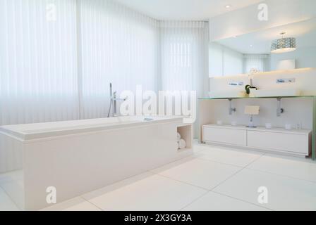 Vasca da bagno rettangolare allungata bianca e armadi con grande specchio a parete nel bagno privato con pavimento in piastrelle di ceramica al piano superiore all'interno di un lussuoso Foto Stock