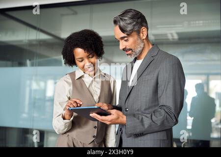 Due partner aziendali professionali soddisfatti e diversificati che lavorano in ufficio con un tablet. Foto Stock