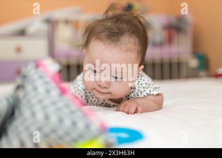 Bambina con la sindrome di Down stai in piedi sulla pancia e guarda un giocattolo Foto Stock