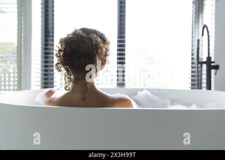 Una giovane donna caucasica che si rilassa a casa nella vasca da bagno e nello spazio per le copie Foto Stock