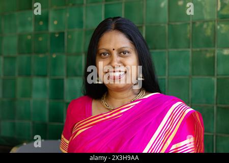 Donna indiana che indossa un sari rosa brillante, in piedi a casa, offrendo un sorriso caldo Foto Stock