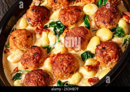 primo piano di polpette di pollo toscano con gnocchi in salsa cremosa con pomodori secchi e foglie di spinaci in piatto da forno Foto Stock