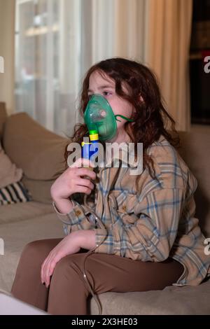 Ragazza malata che fa inalazione con nebulizzatore per ridurre la tosse, a casa, bambino che prende farmaci mentre respira attraverso la maschera facciale. Bronchite e A. Foto Stock