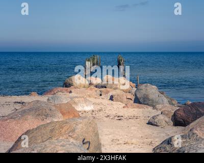 Passeggiando lungo il sentiero sabbioso, si attraversa la bellezza costiera della Lettonia, ripercorrendo le orme della storia fino a un antico molo in cui si trova una sentinella Foto Stock