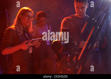 La troupe di produzione video lavora insieme nel backstage con luci al neon rosse, spazio di copia Foto Stock