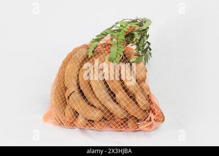 Un sacco di pile di frutti tamarindi con foglie verdi isolate su sfondo bianco. Foto Stock