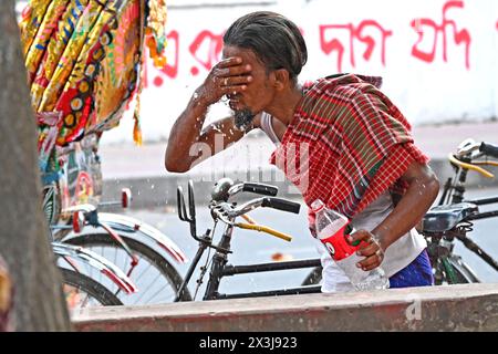 Un autista di risciò che si lava il viso con acqua in un gasdotto lungo la strada durante le ondate di caldo a Dacca, Bangladesh, il 27 aprile 2024 Credit: Mamunur Rashid/Alamy Live News Foto Stock