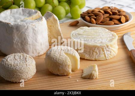 Tagliere di formaggio con formaggio Chaource francese, formaggio Pico di capra e formaggio Crottin de chevre da vicino con uva e mandorle sullo sfondo Foto Stock