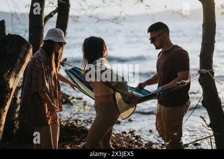 Amici che preparano un'amaca in riva al lago durante un rifugio nella natura Foto Stock