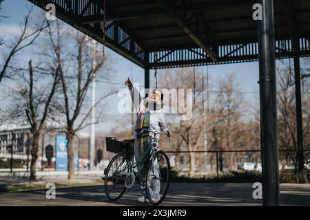 Donna anziana gioiosa con bicicletta rivolta verso l'alto in un parco urbano. Foto Stock