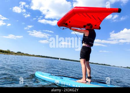 21 aprile 2024: L'uomo naviga con un aliscafo o vela a vela su una tavola SUP o una tavola gonfiabile con il vento in acqua su un lago balneabile al sole *** Mann surft mit einem Wingfoil bzw. Scheda SUP Wind-Segel auf einem Aufblasbarem Surfbrett mit dem Wind im Wasser auf einem Badesee bei Sonnenschein Foto Stock