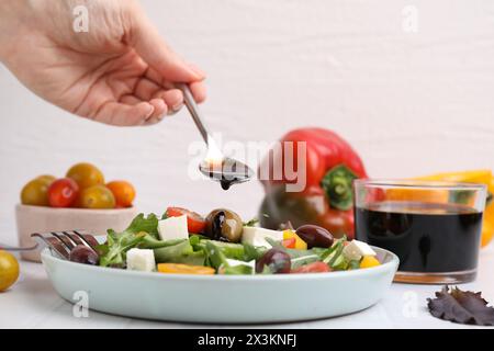 Donna che versa aceto dal cucchiaio al piatto con insalata sul tavolo con piastrelle bianche, primo piano Foto Stock