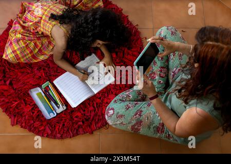 Madre e figlia latinoamericane sedute insieme a fare i compiti a scuola Foto Stock