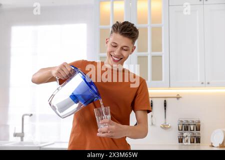 Uomo felice che versa acqua dalla caraffa del filtro in vetro in cucina Foto Stock