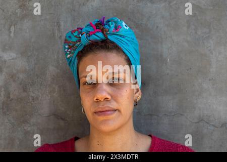 Afro donna latinoamericana (34) con occhi verdi, foulard e isolata su sfondo grigio, guarda direttamente la telecamera con un atteggiamento serio. Foto Stock