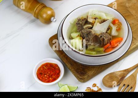 SOP Daging sapi o zuppa di manzo indonesiana, servita su una ciotola bianca in ceramica con sambal e fette di lime. Messa a fuoco selettiva con sfondo in marmo bianco. Foto Stock