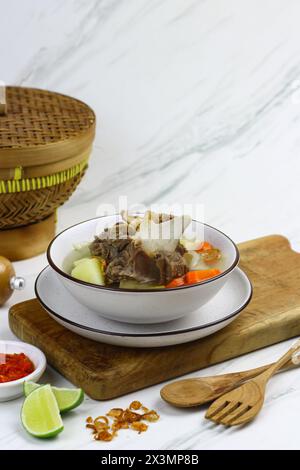 SOP Daging sapi o zuppa di manzo indonesiana, servita su una ciotola bianca in ceramica con sambal e fette di lime. Messa a fuoco selettiva con sfondo in marmo bianco. Foto Stock