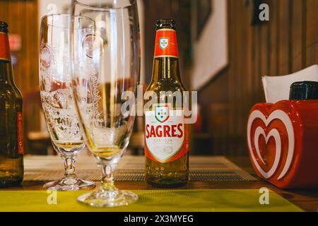 Tavira, Portogallo, 8 gennaio 2024. Bottiglia di birra Sagres su un tavolo con bicchieri da birra vuoti e un dispenser di tovaglioli rosso a forma di cuore in un ambiente accogliente Foto Stock