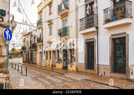 Tavira, Portogallo, 8 gennaio 2024. Strada a Tavira, Portogallo, con pavimentazioni acciottolate, decorazioni sospese e tradizionali edifici bianchi con ir Foto Stock