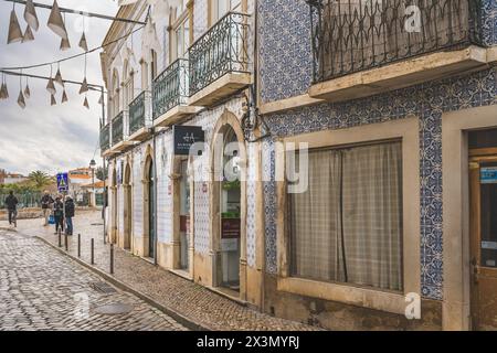 Tavira, Portogallo, 8 gennaio 2024. Una strada acciottolata a Tavira, Portogallo, con una facciata dell'edificio decorata con intricate piastrelle blu e bianche e. Foto Stock