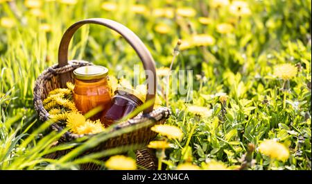 Fiori di dente di leone in un cesto di vimini con un vaso di miele posto a terra da qualche parte in un prato. Foto Stock