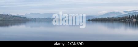 Splendida immagine di paesaggio tranquillo della mattina nebbiosa di primavera su Windermere nel Lake District con barche ormeggiate sul lago e lontane cime nebbiose Foto Stock