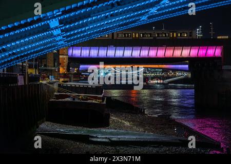 Dettagli dei rivetti e la struttura in acciaio di un ponte londinese sotto che illumina le rive del Tamigi con futuristiche ligh blu e viola Foto Stock