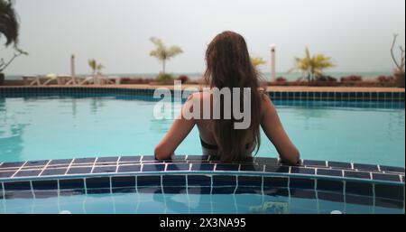 Una donna è seduta in una piscina, di fronte alla macchina fotografica, in un ambiente tropicale in un resort sull'isola di Koh Phangan, Thailandia. Foto Stock
