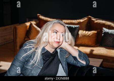 Donna con capelli biondi platino che si rilassa in una giacca in denim al chiuso Foto Stock