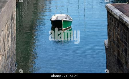 Una barca verde solitaria nelle acque calme di un porto Foto Stock