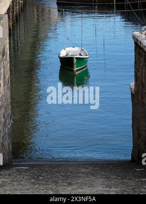 Una barca verde solitaria nelle acque calme di un porto Foto Stock