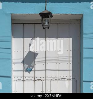 Vecchia lampada di vetro appesa a una parete che crea un motivo gettando un'ombra sul muro dietro, nelle strade secondarie della città vecchia, Trinidad, Cuba. Foto Stock