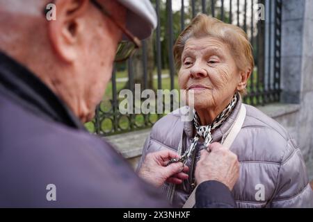 un vecchio aiuta sua moglie a vestirsi fuori. famiglia unita in vecchiaia Foto Stock