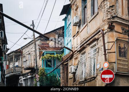 Una strada stretta e intemprata a Tbilisi, Georgia, caratterizzata da balconi colorati, facciate antiche e un groviglio di cavi sospesi Foto Stock
