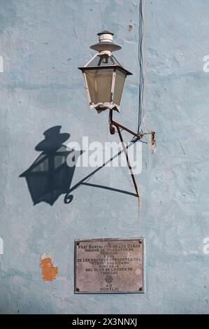 Vecchia lampada di vetro appesa a una parete che crea un motivo gettando un'ombra sul muro dietro, nelle strade secondarie della città vecchia, Trinidad, Cuba. Foto Stock