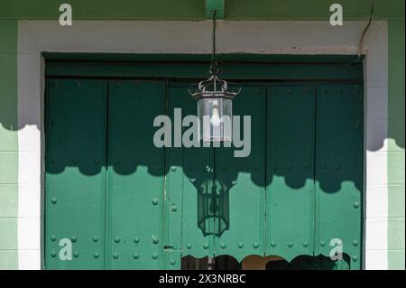 Vecchia lampada di vetro appesa a una parete che crea un motivo gettando un'ombra sul muro dietro, nelle strade secondarie della città vecchia, Trinidad, Cuba. Foto Stock