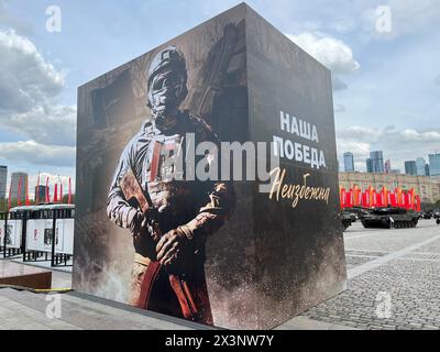 28 aprile 2024, Russia, Moskau: In una mostra al Pobedy Park (Parco della Vittoria) con trofei di guerra dall'Ucraina, un cubo con l'immagine di un soldato russo e l'iscrizione: "La nostra vittoria è inevitabile!" si trova all'ingresso. Sulla destra c'è un carro armato da battaglia tedesco Leopard 2 catturato in Ucraina, secondo fonti russe. Sullo sfondo ci sono dei segnali d'allarme con l'iscrizione Pobeda! (In tedesco: Vittoria). Il 9 maggio, la Russia celebra il giorno della vittoria dell'Unione Sovietica sulla Germania nazista nella seconda guerra mondiale. La nuova mostra nel parco è dedicata all'offensiva russa contro il Regno Unito Foto Stock