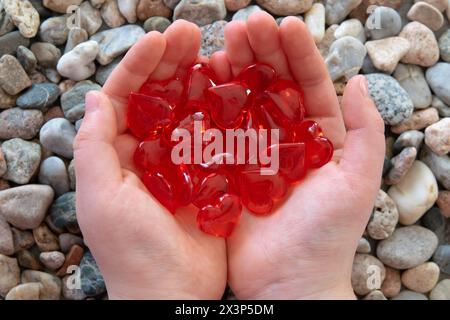 Cuori di vetro rosso brillante nelle mani dei bambini sullo sfondo delle pietre. Concetto di San Valentino e amore romantico. Foto Stock