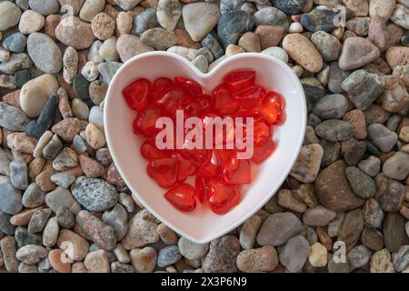 Cuori di vetro rosso brillante in un romantico piatto a forma di cuore su pietre di ciottoli. Foto Stock