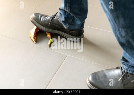 Primo piano di un uomo con scarpe nere che si accostano a una buccia di banana mentre cammina. Concetto di pericolo di inciampare o cadere. Solo piedi visibili. Foto Stock