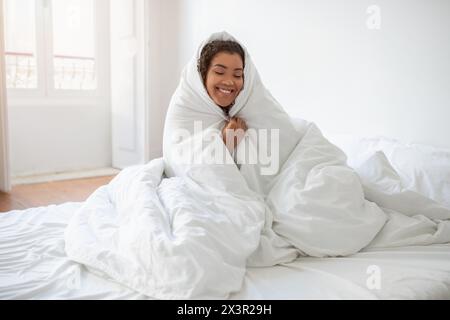 Donna sorridente avvolta in coperta a letto Foto Stock