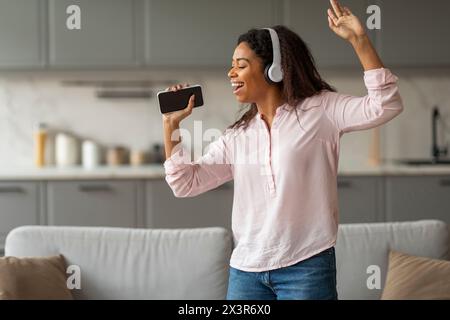 Felice giovane donna nera con le cuffie che cantano Foto Stock