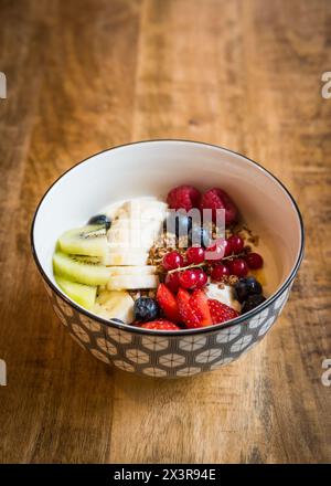 Ciotola di yogurt fresco con muesli, bacche estive miste, banana e kiwi su un tavolo di legno Foto Stock