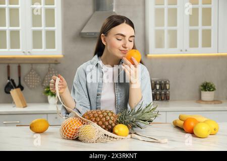 Donna con un sacchetto di frutta fresca al tavolo di marmo chiaro in cucina Foto Stock