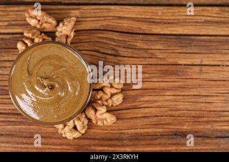 Delizioso burro di noci nel recipiente e noci sul tavolo di legno, vista dall'alto. Spazio per il testo Foto Stock